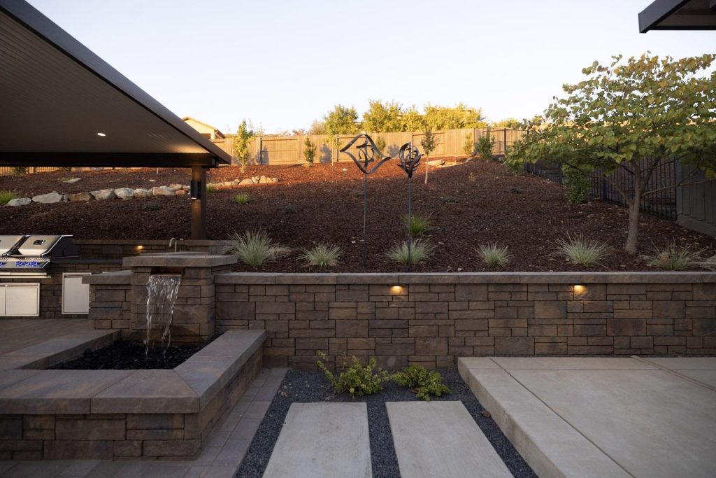 Stone block retaining wall with a water feature in a landscaped backyard